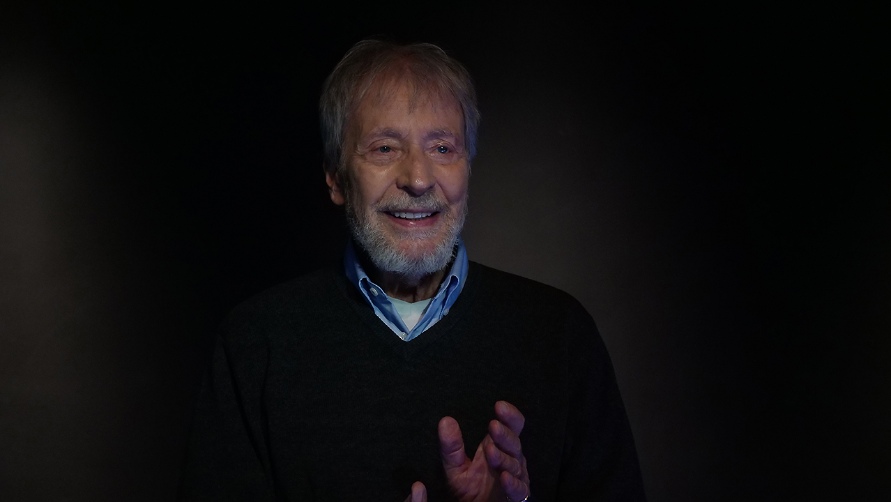 Wolfgang Keuter Wolfgang Keuter im schwarzen Bühnenraum. Er trägt ein hellblaues Hemd und einen schwarzen Pulli. Sein Blick ist nach vorne rechts gerichtet. Er zeigt einen freundlichen und interessierten Gesichtsausdruck.